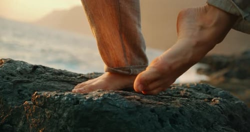 Bare feet of woman dancing on volcanic rock during coastal sunset