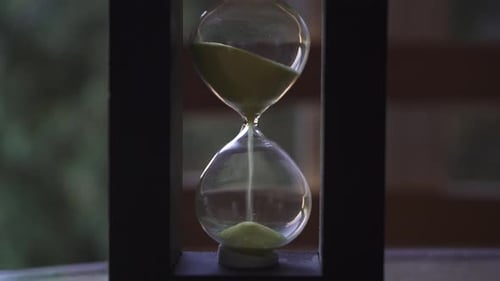 Hourglass with yellow sand falling down on a wood table