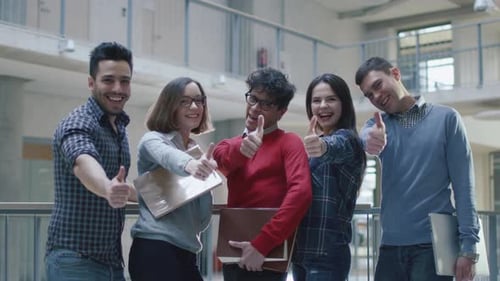 Group of happy young multi-ethnic students are showing thumbs-up in a college building.