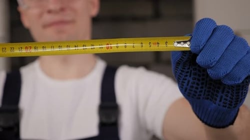 A Construction Worker in a Helmet and Glasses Holding a Measuring Tape Measure
