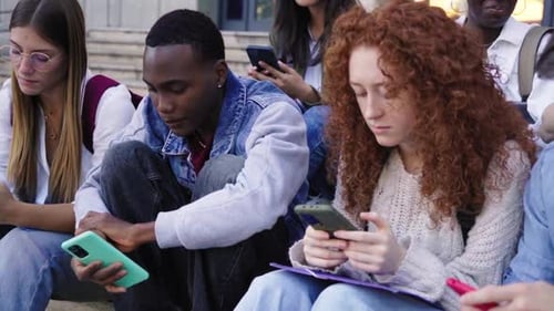 Multiracial Group of Students Sitting Outside University Using Phones Concentrated in Social Media