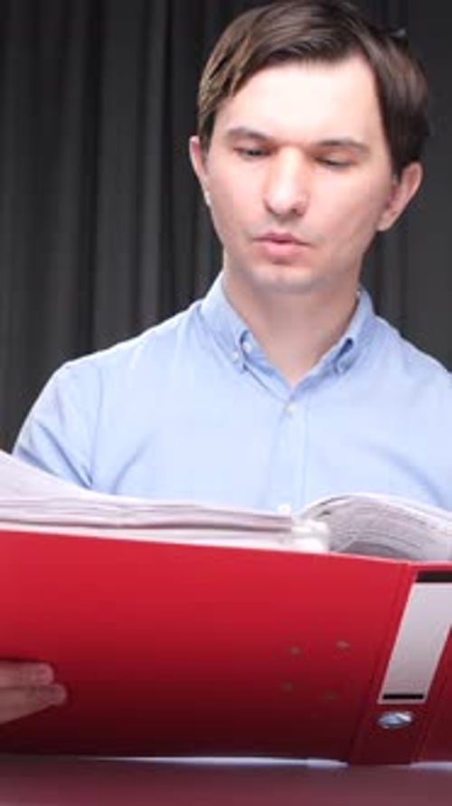 Vertical Video Office Worker Reading Documents in a Red Folder at Night