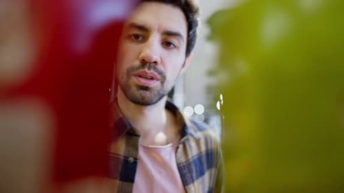 Close Up a Confident Brunette Guy with Stubble in a Checkered Shirt Approaches the Counter in a