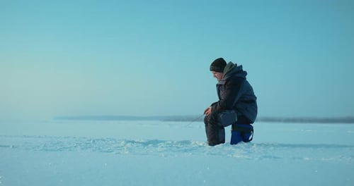 Man Ice Fishing on Frozen Snowy Lake in Winter