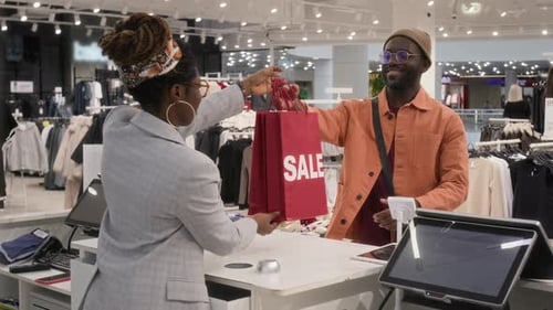 Clothes Store Cashier Handing Bags with Sale Sign to Customer