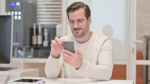 Young Man Celebrates Success with Smartphone in Office