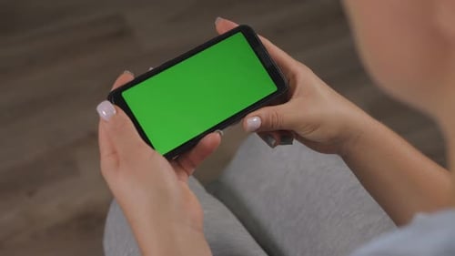 Closeup of a Woman Holding a Phone with a Green Screen at Home on the Couch