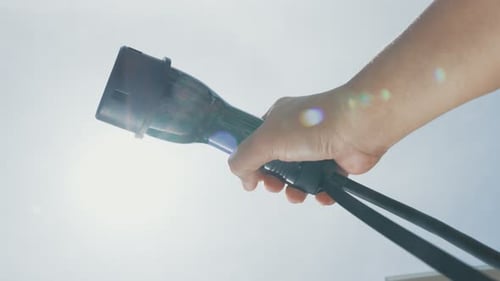 Nahaufnahme mit der Hand, die einen EV-Stecker für Elektrofahrzeuge als fortschrittliche Idee fasst.
