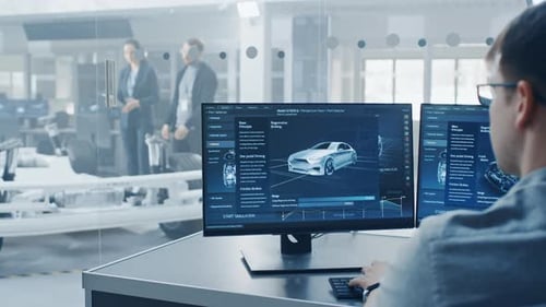 Professioneller Ingenieur arbeitet an einem Computer mit einer 3D-Software, während Kollegen das Elektroauto inspizieren
