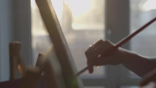 Artist Painting on Canvas with Brush in Golden Light