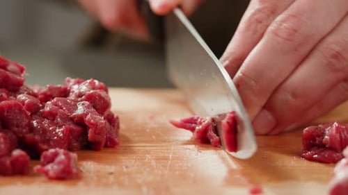 Hands Cutting Raw Meat on a Wooden Board