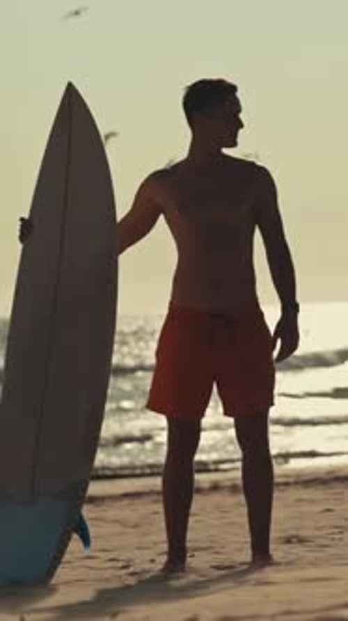 Surfer Holding Surfboard on Beach at Sunset