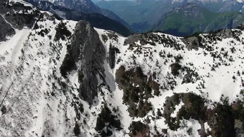 Vista de Zumbido en Albania, en los Alpes, volando sobre un pico montañoso nevado y rocoso y hacia un bosque verde