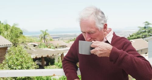 Senior Man Drinking on Balcony Overlooking Garden