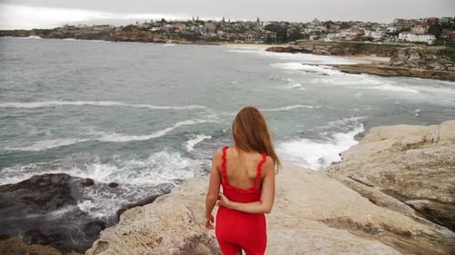 Girl In Red Dress Walks Barefoot On The Rocks - Girl Stands On The Rock Watches The Crashing Waves -