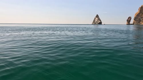 Sea Water Surface Camera Flies Over the Calm Azure Sea with Volcanic Rocky Shores on Background