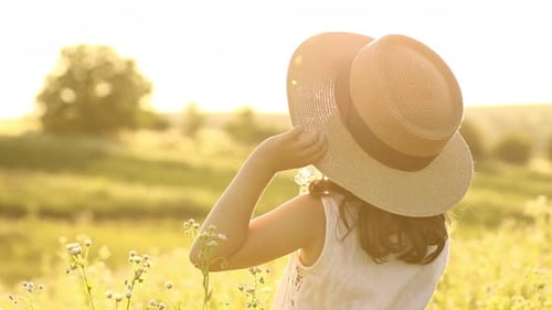 View of adorable smiling child girl in straw hat on summer meadow with high grass. Little joyful kid