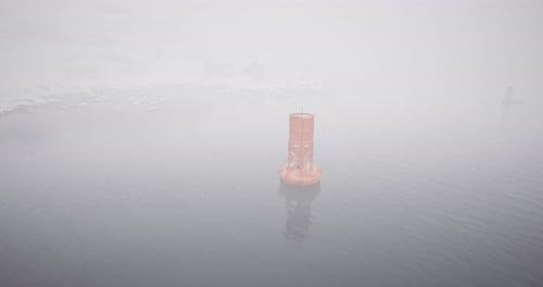 Día de niebla con una boya solitaria de pie en aguas tranquilas