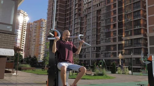 A Young Man with Thin Skin Body is Training on Arm Trainer on a Street Sports Ground in a Beautiful
