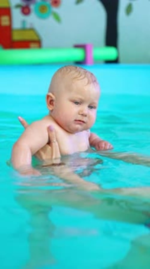 Trainer holds a baby in the swimming pool on the straight hands.