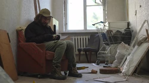 Homeless Poor Man Sitting in a Room of an Abandoned Building Filled with His Meager Belongings He