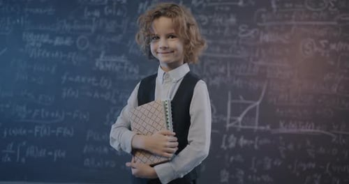 Young Boy Holding Notebooks In Front of Chalkboard