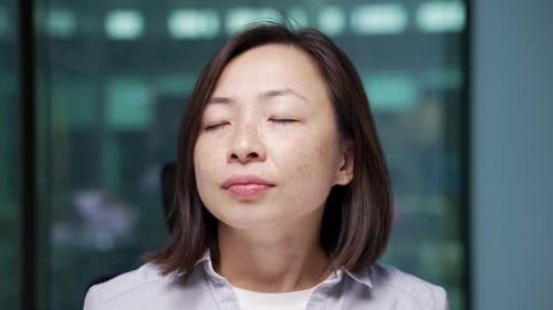 Asian businesswoman relaxing with her eyes closed sitting at workplace in a modern business office.