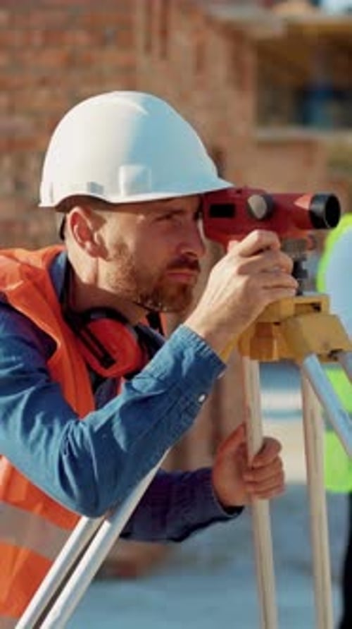 Construction Worker Uses Surveying Instrument on Building Site
