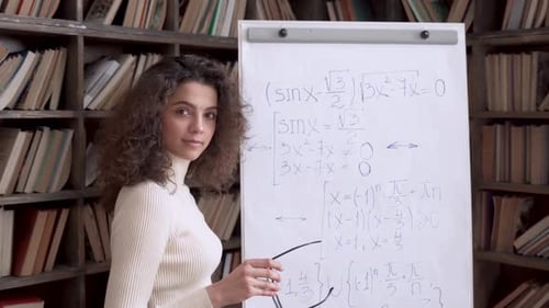 Smiling hispanic math teacher explains equation at whiteboard in university classroom