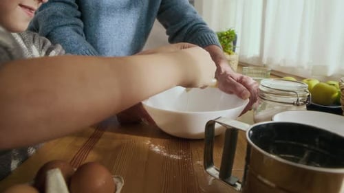 Grandfather and Grandson Cracking Eggs into Bowl while Baking Together
