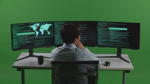 Back View Of Asian Man Thinking While Write Code With Multiple Computer Screens In Green Screen