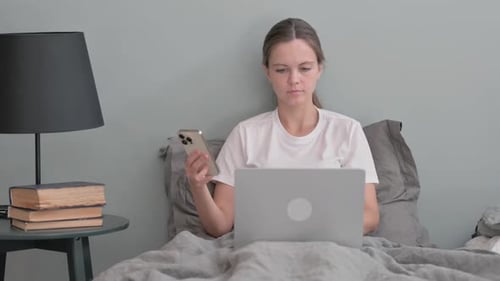 Woman Uses Laptop and Phone in Bed