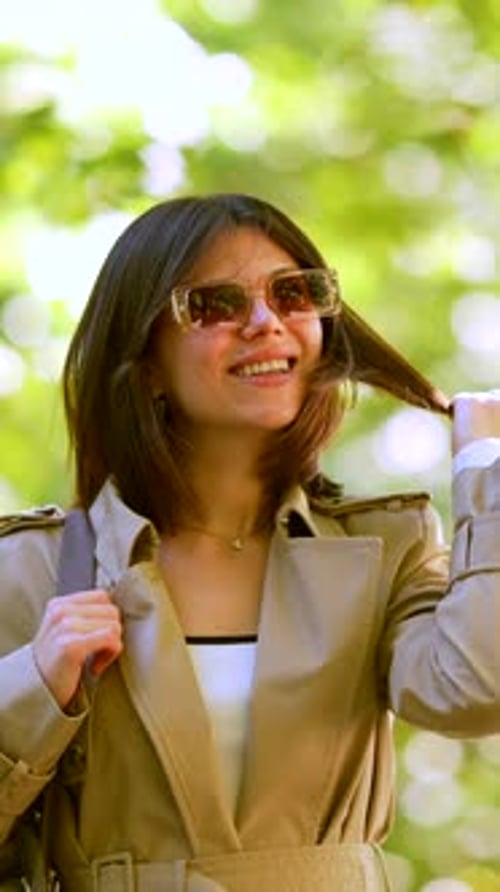 A Woman Wearing a Tan Coat and Sunglasses Walks Down a Path