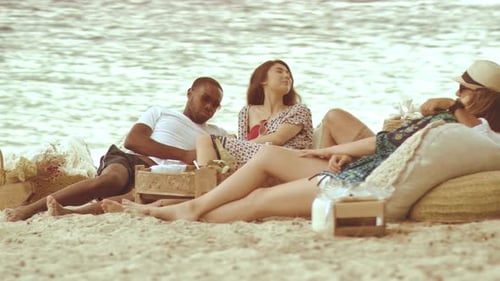 Millennial friends enjoy golden hour beach picnic in sunny tropical Australia