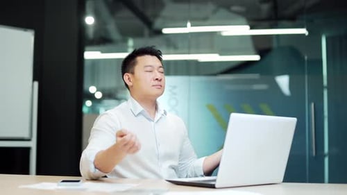 Asian business man meditating. Successful businessman meditates sitting at table in modern office,