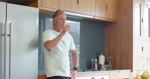 Reifer Mann hebt klares Glas und trinkt, während er den Durst an der Küchentheke stillt