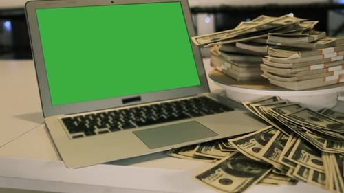 Many stacks 100 US dollars bills near laptop with chromakey on white table in office night time