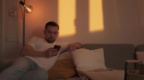 Man Relaxing on Sofa Uses Smartphone