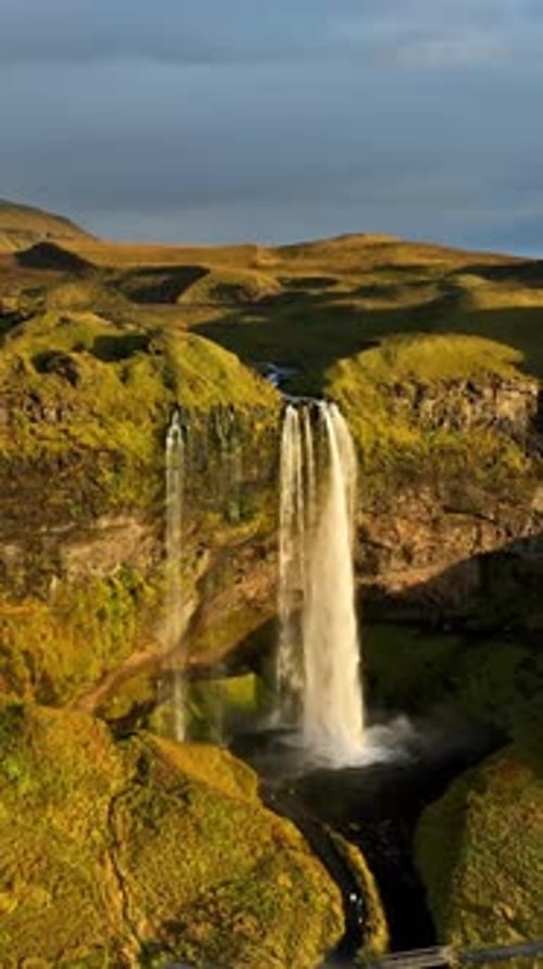 Vue aérienne verticale de Seljalandsfoss en Islande avec une cascade imposante, des falaises sculptées et des rayons lumineux