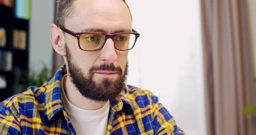 Close Up of Caucasian Handsome Man in Glasses and with Beard Sitting in Front of Laptop Screen and