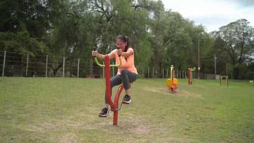 The Woman is Utilizing a Pedal Exercise Equipment in the Park - Wide Shot