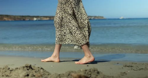 Tourist Woman Steps Along Beach with Bare Feet While Skirt Moves Beside Surf