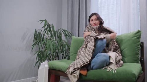 Woman with Blanket Sitting on Couch Rubbing Hands