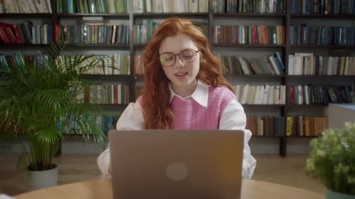 Young Woman Using Laptop in Front of Bookshelves