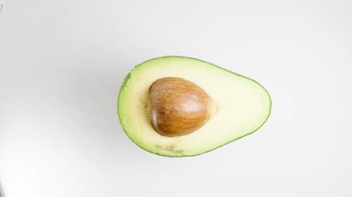 Precisely Cut Avocado Half with Pit Rotates on a White Background, Looping. Top View, Isolated.