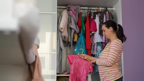 Woman Styling Children's Clothes in Bedroom Closet