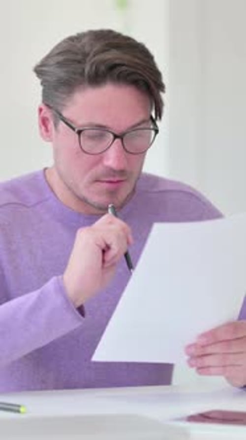 Man Reviews Documents at Desk Indoors, Thinking Hard
