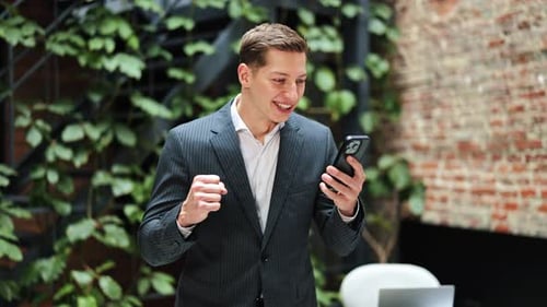 Excited Businessman Celebrates Success After Receiving Good News on Phone in Office
