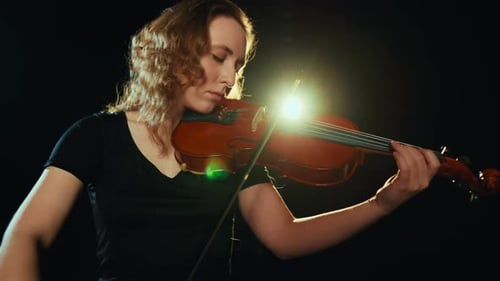 Woman Focused on Violin Performance in Dark Studio