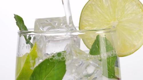 Close Up Of Fresh Lime Soda Being Poured Into A Glass With Mint, Sliced Lime, And Ice